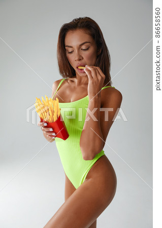 Sporty woman eating unhealthy food on light background. Diet concept 86658560