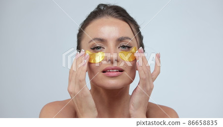 Beauty portrait of healthy shirtless woman wearing cosmetic gold patches under her eyes isolated over gray background. 86658835