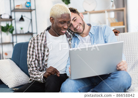 Two multiracial men in relationship using laptop on couch Two multiracial men in relationship using laptop on couch 86658842