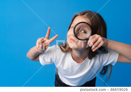Little girl looking through a magnifying glass on blue background 86659026