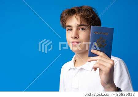 Portrait of glad handsome boy showing his passport going on vacation against blue background Portrait of glad handsome boy showing his passport going on vacation against blue background 86659038