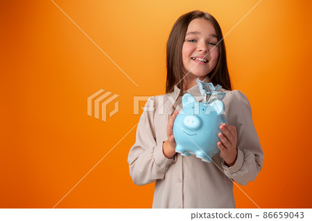 Teen girl with piggy bank on orange color background. Teen girl with piggy bank on orange color background. 86659043