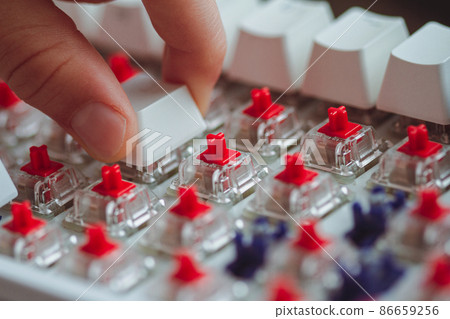 fingers placing a keycap on a white mechanical keyboard 86659256
