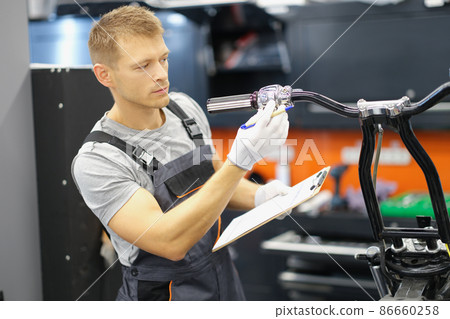 Garage service worker check wheel on motorbike, hold clipboard with info Garage service worker check wheel on motorbike, hold clipboard with info 86660258