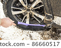 Cleaning a dirty car wheel with a brush scraper from dirt and snow on a sunny frosty winter morning. 86660517
