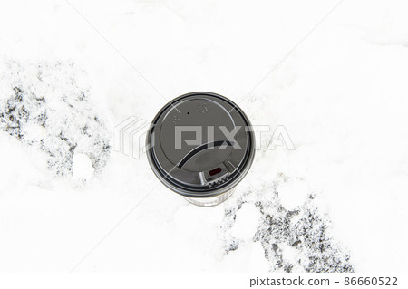 A large disposable paper cup with a lid for hot drinks on a snowy background. A large disposable paper cup with a lid for hot drinks on a snowy background. 86660522
