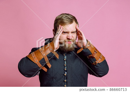 Portrait of young bearded man in image of medieval warrior, archer suffering from pain, touching temples in headache isolated over pink background Portrait of young bearded man in image of medieval warrior, archer suffering from pain, touching temples in headache isolated over pink background 86660713