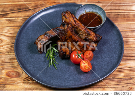 Spicy hot grilled spare ribs from a summer BBQ served with a hot chili pepper and fresh tomatoes on an old vintage wooden cutting board. Spicy hot grilled spare ribs from a summer BBQ served with a hot chili pepper and fresh tomatoes on an old vintage wooden cutting board. 86660723