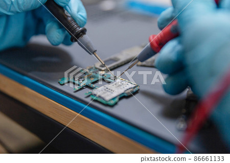 Phone repair concept a young electrical technician using an ammeter measuring the current in a circuit of an electronic device Phone repair concept a young electrical technician using an ammeter measuring the current in a circuit of an electronic device 86661133