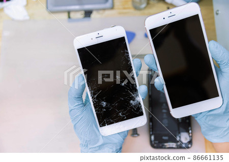 Phone repair concept two hands wearing rubber gloves holding two smartphones in different conditions; the good one and the broken one Phone repair concept two hands wearing rubber gloves holding two smartphones in different conditions; the good one and the broken one 86661135