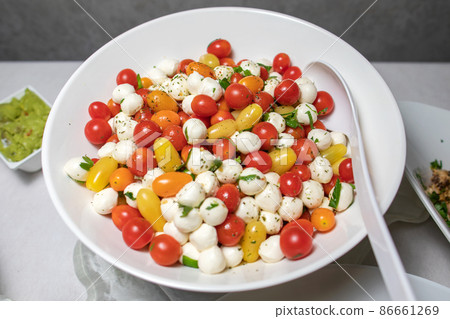 Italian tricolore, small balls of fresh white soft Italian mozzarella cheese, ripe red cherry tomatoes and fresh green basil herb, ready for making caprese salad, close up. Italian tricolore, small balls of fresh white soft Italian mozzarella cheese, ripe red cherry tomatoes and fresh green basil herb, ready for making caprese salad, close up. 86661269