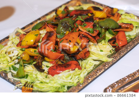 Roasted yellow and red bell pepper salad with capers and olives in a blue bowl on a white background. Grilled vegetables. Roasted yellow and red bell pepper salad with capers and olives in a blue bowl on a white background. Grilled vegetables. 86661384