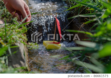 A man lowers a child's boat into a narrow canal or stream.  86661573