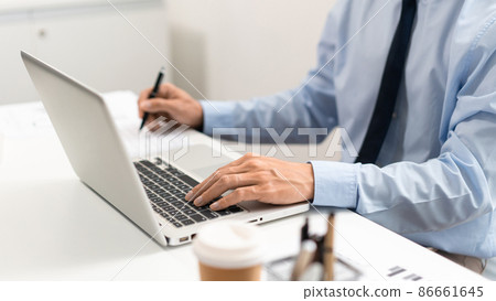 Working Man Conept The male officer sitting in the office, laying his left hand on the laptop, and writing something on the paper with his right hand 86661645
