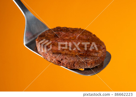 Meat steak on barbecue grilling tool - spatula handle on yellow wall. Cooking beef or pork patty Meat steak on barbecue grilling tool - spatula handle on yellow wall. Cooking beef or pork patty 86662223
