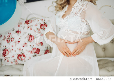 Pregnant woman in white holding hands on stomach 86662288