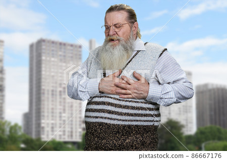 Senior man clutching his chest because of terrible pain standing on city buildings background. 86667176