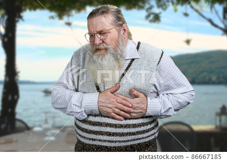 Old caucasian man suffering from heart ache standing outdoors. Old caucasian man suffering from heart ache standing outdoors. 86667185
