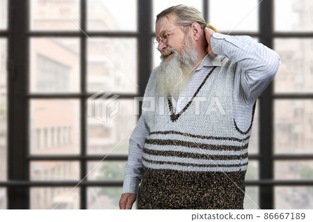 Old bearded man suffering from nape pain standing on windows background. 86667189