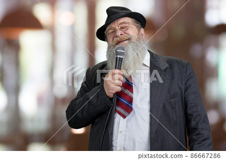Old elegant man talking in microphone on abstract bokeh background. Old elegant man talking in microphone on abstract bokeh background. 86667286