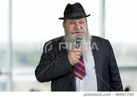 Elderly bearded businessman in suit talking into microphone. Elderly bearded businessman in suit talking into microphone. 86667298