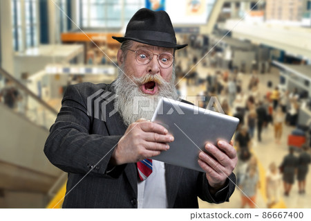 Shocked senior businessman using digital tablet while standing on escalator at airport. Shocked senior businessman using digital tablet while standing on escalator at airport. 86667400