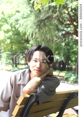 一個年輕人看著相機在公園裡放鬆 一個年輕人看著相機在公園裡放鬆 86668004
