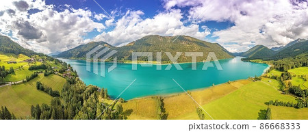 Drone panorama over turquoise lake Weissensee in Austrian province of Carinthia during daytime Drone panorama over turquoise lake Weissensee in Austrian province of Carinthia during daytime 86668333