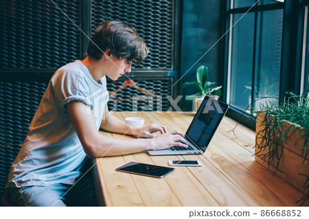 Serious man browsing laptop located on wooden table with gadgets 86668852