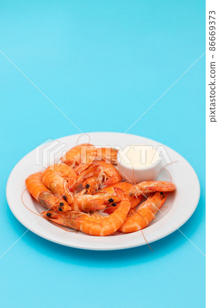 Boiled fresh shrimps with sauce in small bowl on white plate on blue Boiled fresh shrimps with sauce in small bowl on white plate on blue 86669373