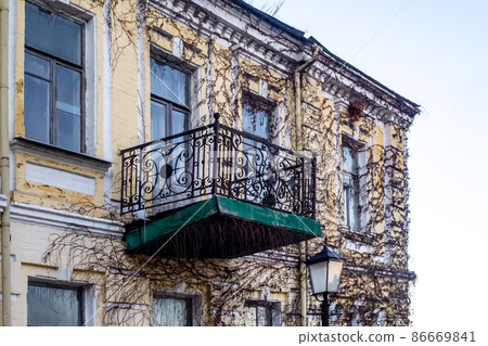 Elegant old ruined balcony with wrought iron railings on facade of an abandoned building in Kiev, Ukraine. .View on facade of an abandoned house with ornate wrought iron railings on balcony. Elegant old ruined balcony with wrought iron railings on facade of an abandoned building in Kiev, Ukraine. .View on facade of an abandoned house with ornate wrought iron railings on balcony. 86669841