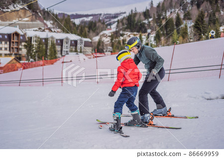 Boy learning to ski, training and listening to his ski instructor on the slope in winter Boy learning to ski, training and listening to his ski instructor on the slope in winter 86669959