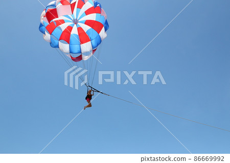 A woman is gliding using a parachute on the background of cloudy blue sky. 86669992