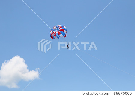 A woman is gliding using a parachute on the background of cloudy blue sky. 86670009