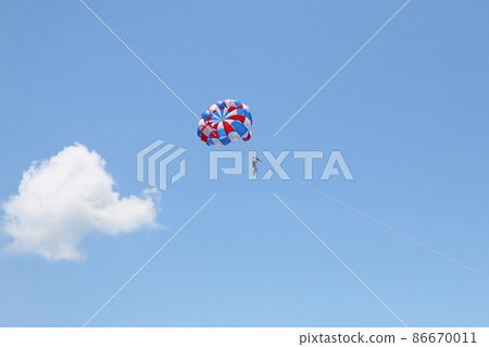 A woman is gliding using a parachute on the background of cloudy blue sky. 86670011