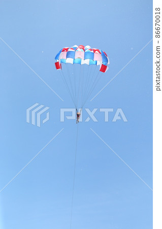 A woman is gliding using a parachute on the background of cloudy blue sky. 86670018