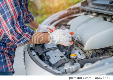 Asian auto mechanic check for repair under the hood of broken down car on the side of the road. 86671459