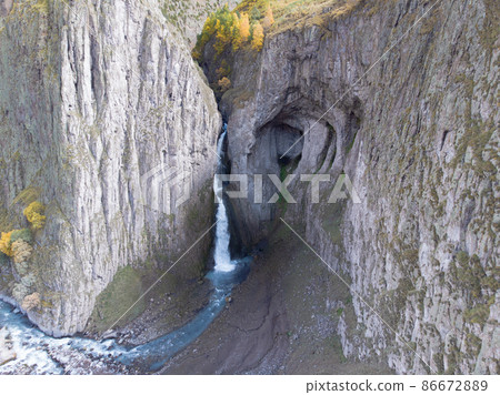 Aerial view of the big waterfall, Caucasus. Powerful stream of clean water runs from the melting glacier, falls down from the mountains and the blue river flows. Harsh rocks all around. Wild nature 86672889