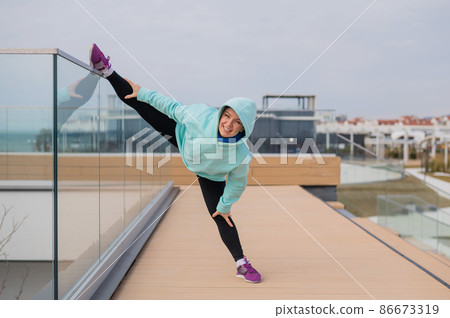 Caucasian woman in a sweatshirt stretches on the twine outdoors.  86673319