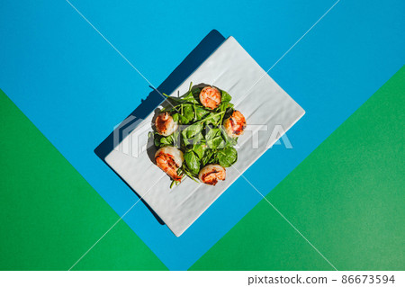 Salad with shrimps and arugula on white dish on colored background Salad with shrimps and arugula on white dish on colored background 86673594