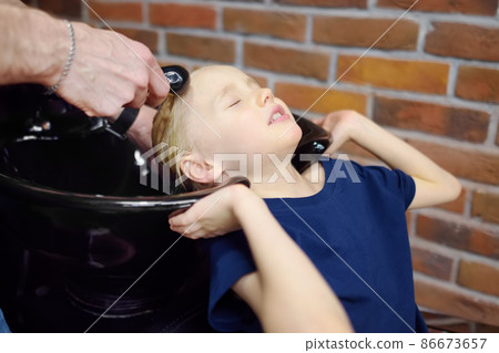 Preschooler boy getting haircut in barbershop. Children hairdresser washing hair for child. Cutting hair for kids Preschooler boy getting haircut in barbershop. Children hairdresser washing hair for child. Cutting hair for kids 86673657