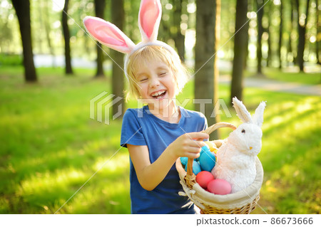 Little boy wearing bunny ears costume hunting for eggs in spring garden on Easter day. Traditional easter festival outdoors. 86673666