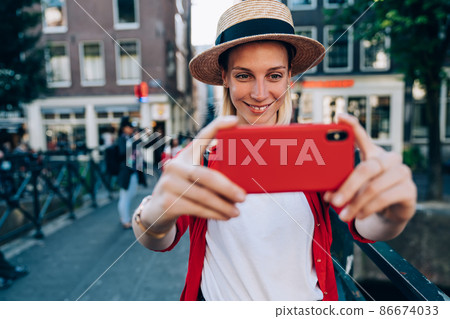 Positive female traveler taking self photo on cellphone in town 86674033
