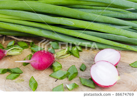 Fresh green onions, red radish on cutting board. 86674769