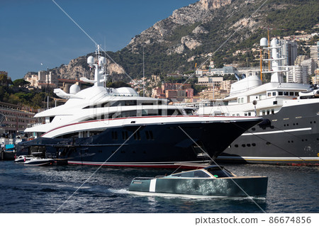 A lot of huge yachts are in port of Monaco at sunny day, Monte Carlo, mountain is on background, glossy board of the motor boat, megayachts are moored in marina, sun reflection on glossy board 86674856