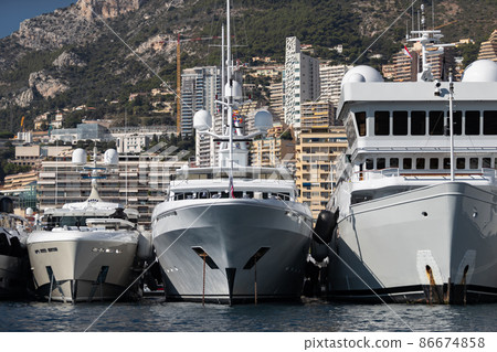 A lot of huge yachts are in port of Monaco at sunny day, Monte Carlo, mountain is on background, glossy board of the motor boat, megayachts are moored in marina, sun reflection on glossy board 86674858