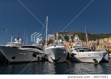 A lot of huge yachts are in port of Monaco at sunny day, Monte Carlo, mountain is on background, glossy board of the motor boat, megayachts are moored in marina, sun reflection on glossy board 86674861