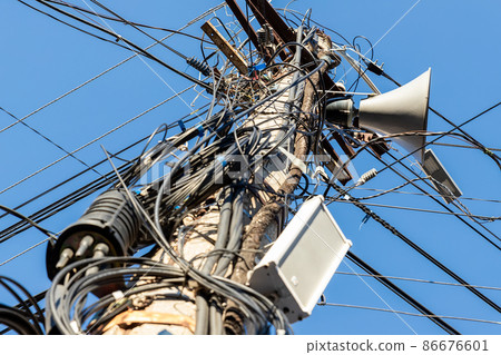 Chaos of many different data cables and network wires messy tangled hanged on concrete pillar pole on urban city street against clear blue sky on day time. Announcement speaker mounted on column Chaos of many different data cables and network wires messy tangled hanged on concrete pillar pole on urban city street against clear blue sky on day time. Announcement speaker mounted on column 86676601