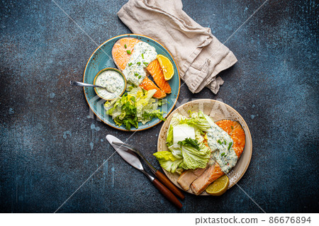 Healthy food meal grilled salmon steaks with dill sauce and salad leafs on two plates Healthy food meal grilled salmon steaks with dill sauce and salad leafs on two plates 86676894