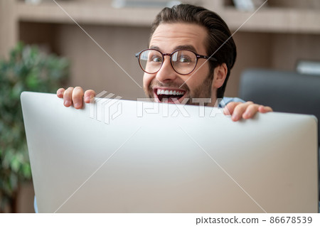 A dark-haired man hiding behind the computer and smiling 86678539